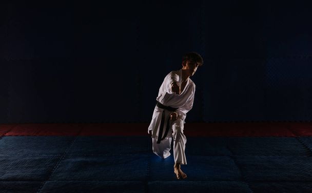 Silhouet van een jongeman met een zwarte band die karate doet in de studio - Foto, afbeelding