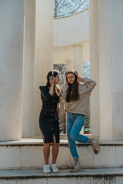 Две девушки веселятся на улице. Они слушают музыку в наушниках и танцуют. - Фото, изображение
