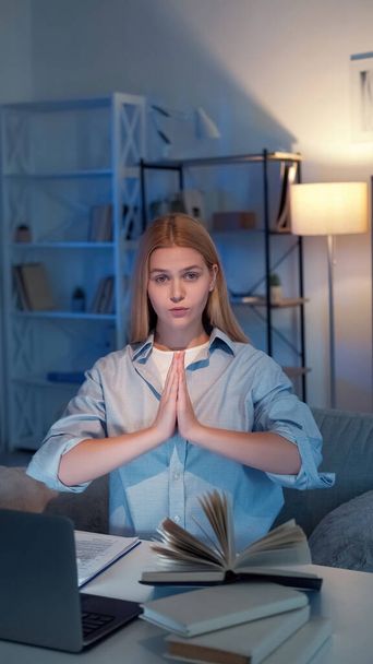 Praying gesture. Peaceful woman. Perfect student. Calm lady ready for exam holding hands together sitting with books laptop in light room interior. - Foto, Bild