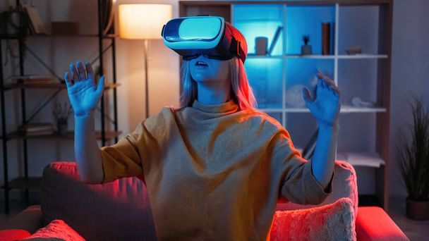 Female gamer. Virtual reality. New experience. Amazed woman in vr goggles looking surprised playing cyber game in dark neon light home interior. - Photo, Image