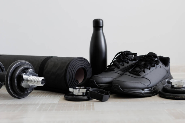 Fitness téma súlyzókkal, sport szőnyeggel, cipővel és vizes palackkal a fapadlón - Fotó, kép