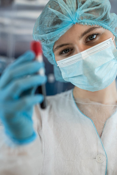 Une femme scientifique en tissu protecteur tient et analyse des éprouvettes avec du sang en laboratoire clinique. Concept - Photo, image