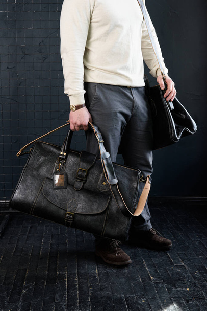 un homme avec des sacs. deux sacs de voyage en cuir noir de taille différente, photo d'intérieur sur fond noir. - Photo, image