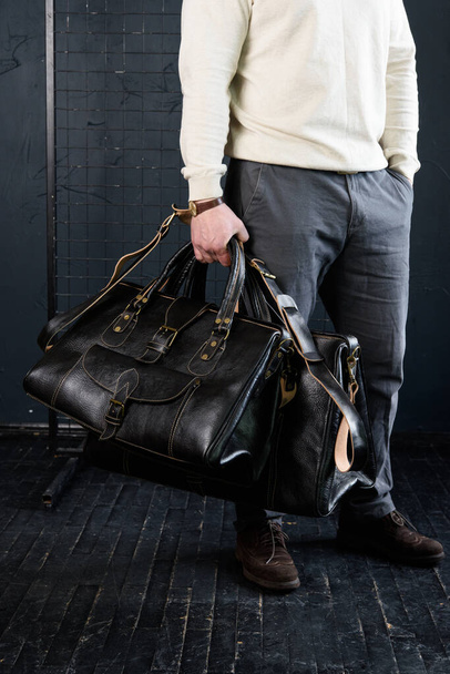 a man with bags. two different size black leather travel bags, indoors photo on black background. - Foto, Bild