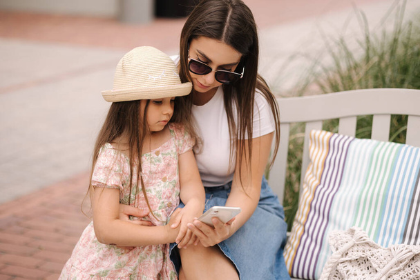 Mom and daughter looking pictures on phone. Beautiful girls using phone outdoor. High quality photo - Zdjęcie, obraz