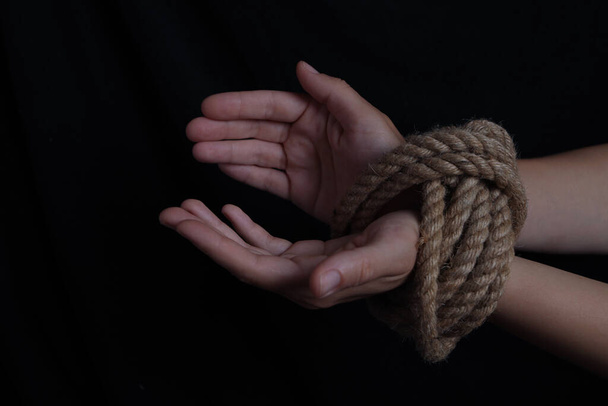 manos de niña atadas con una cuerda sobre un fondo negro - Foto, Imagen