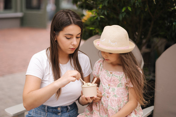 Little girl eating ice cream with mother. Two girls have rest after shopping. Daughter and mom sitting outdoors. High quality photo - Photo, Image