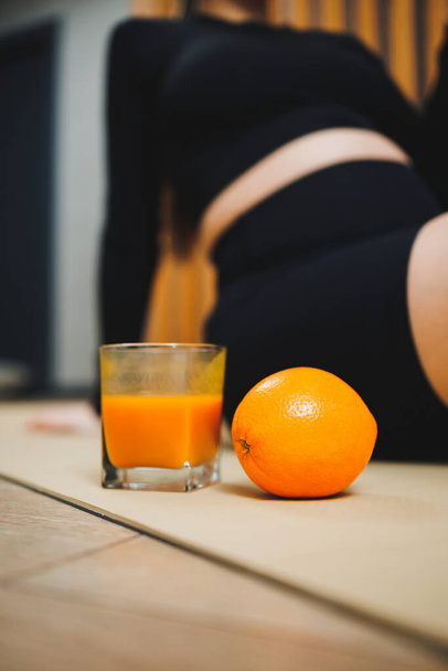 Genç bir kadının arka planında bir bardak taze sıkılmış portakal suyu. Bir kadın vücudu için yararlı bir meyve suyu. Taze narenciye vitamini - Fotoğraf, Görsel