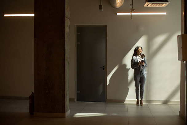 Pretty young business woman using mobile phone in the office hallway - Foto, Imagem