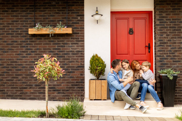 Famille avec une mère, un père, un fils et une fille assis dehors sur les marches d'un porche d'une maison en brique - Photo, image