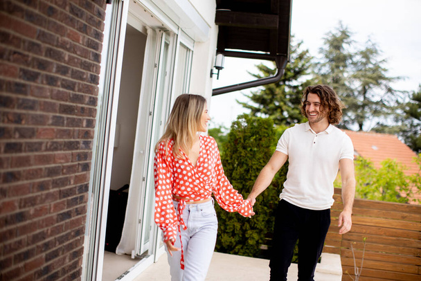 Handsome ymiling young couple in love walking in front of house brick wall - Photo, Image