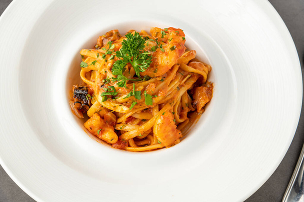 Спагетти с креветками на белой фарфоровой тарелке на черном каменном столе - Фото, изображение