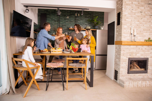 Due famiglie felici che brindano con sidro mentre preparano la cena in cucina - Foto, immagini