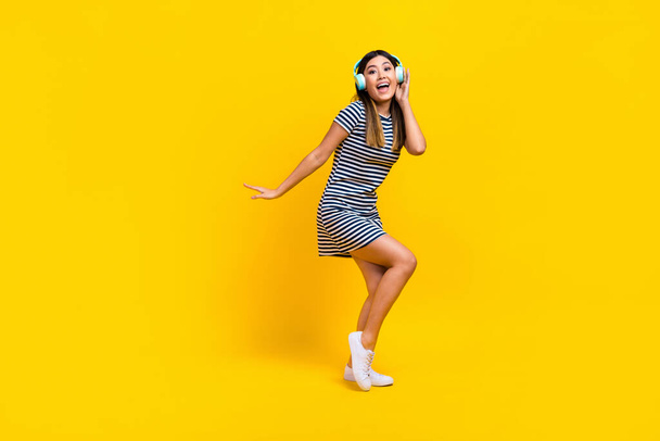 Full length photo of funky cheerful lady wear striped dress dancing listening songs empty space isolated yellow color background. - Foto, imagen