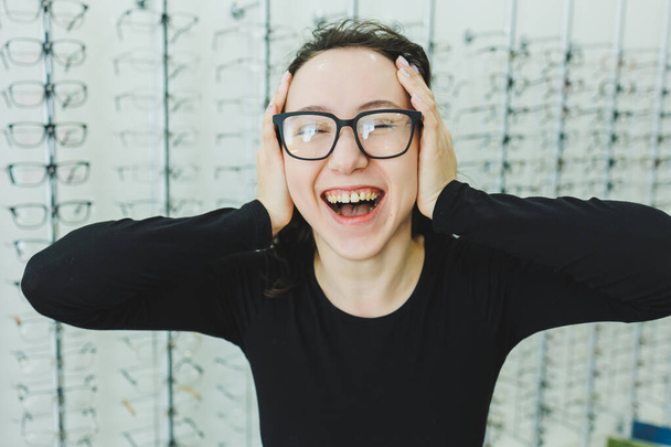 Eine junge Frau wählt in einem Optikgeschäft eine Brille. Mit Brille stehen. Sehkorrektur. Frau mit Brille. Porträt einer Frau mit Korrekturbrille. - Foto, Bild