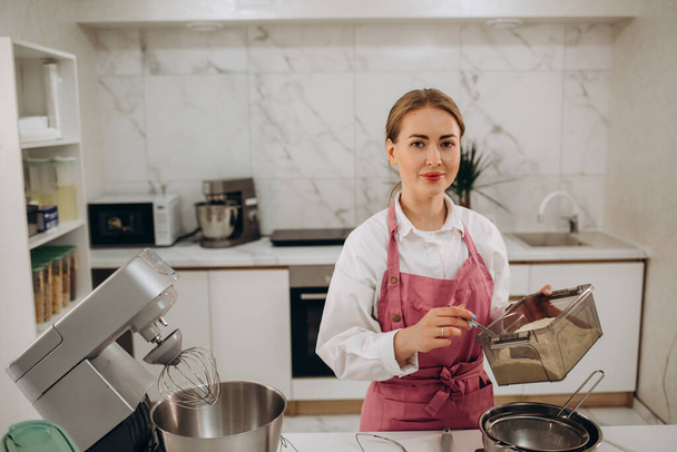 Beautiful young woman prepares sweet pastries in a modern kitchen. - Foto, afbeelding