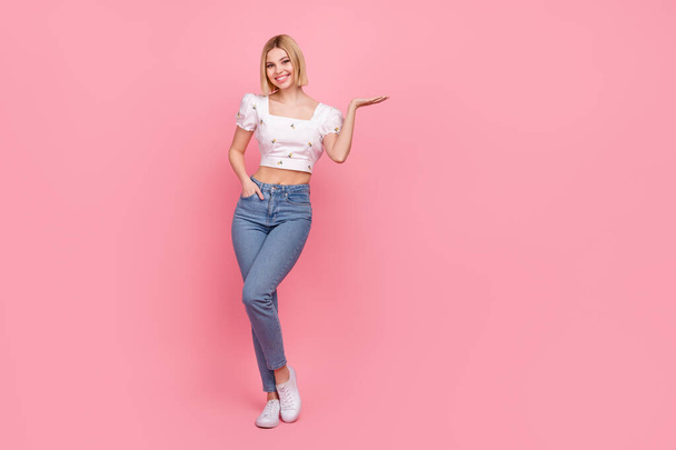 Full body photo of charming blond hair lady hold hand open palm show novelty wear shirt jeans shoes isolated pink color background. - Foto, afbeelding