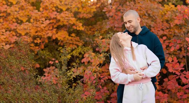 秋の公園で幸せなカップル。秋だ。黄色の木々や葉の背景に若い愛情のある家族。自由の概念。コピースペース。バナー - 写真・画像