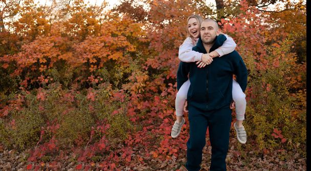 Happy couple in love newlyweds in sports clothes walk in the autumn forest. Young smiling family enjoying fall in the park. Copy space - Фото, зображення