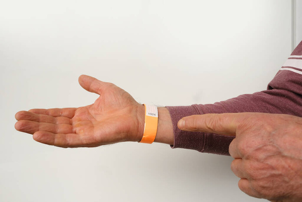 orange paper wristband mockup on persons arm. Clear adhesive bangle wristlet sticker with entry number on male hand of middle-aged european man, blue paper bracelet, check tape, event ticket concept - Photo, Image