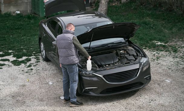 A man stands in front of a car hood.  Man fixing the car on the porch - Φωτογραφία, εικόνα