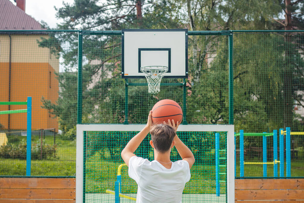 Jonge getalenteerde basketbalspeler is basketballen op zijn buitenbaan en training voor toekomstige games en moeilijke situaties. Ik bereid me voor op het seizoen. Schiet op de mand.. - Foto, afbeelding
