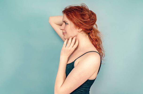Profile of a girl with brown eyes. Hand touches chin. Long red hair, black dress. Gray background - Photo, image
