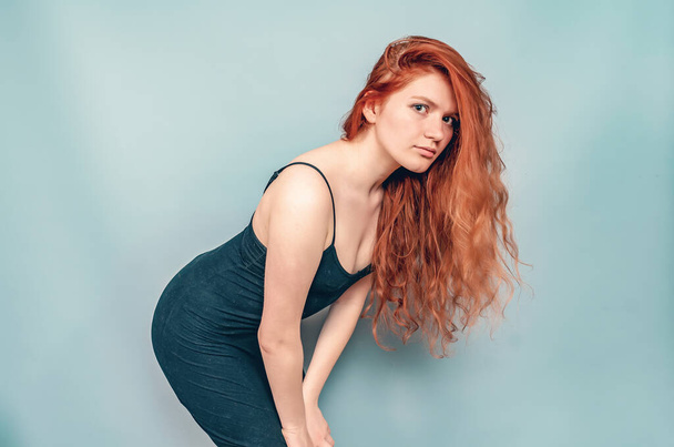 Sexy red-haired woman in black short dress posing on gray background. Studio photo - Photo, Image