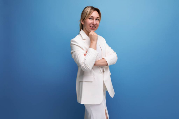 jong zelfverzekerd vrij slanke blonde baas vrouw in een elegante jas en jurk op een blauwe achtergrond met kopieerruimte. - Foto, afbeelding