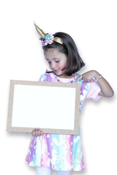 Ребенок в костюме единорога с белой доской и белым фоном. - Фото, изображение
