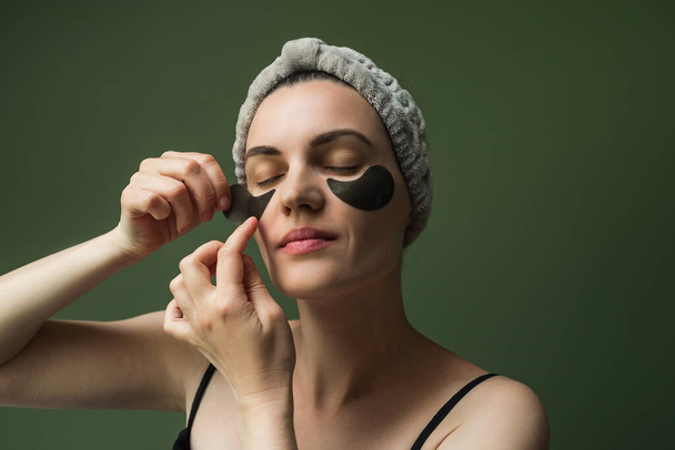 Una mujer europea madura aplica o elimina parches hidratantes debajo de sus ojos. Cuidado de la piel en casa. Piel madura, cosmetología. - Foto, imagen