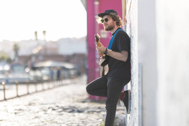 Duvarın yanında duran ve elektro gitar çalan bir hippi. Orta çekim - Fotoğraf, Görsel