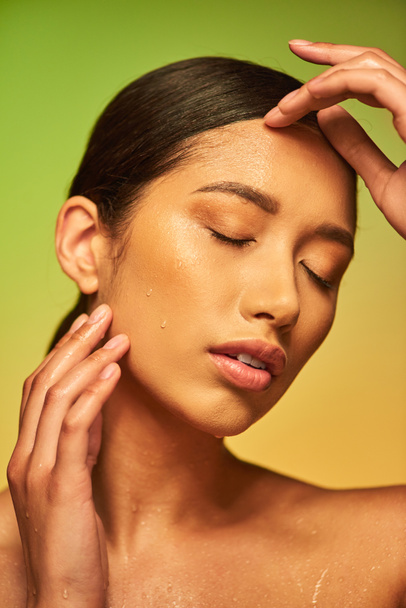water druppels op het gezicht, close-up van jonge Aziatische vrouw met gesloten ogen en natte huid op groene achtergrond, hydratatie van de huid, schoonheidscampagne, perfectie, wellness, conceptuele  - Foto, afbeelding