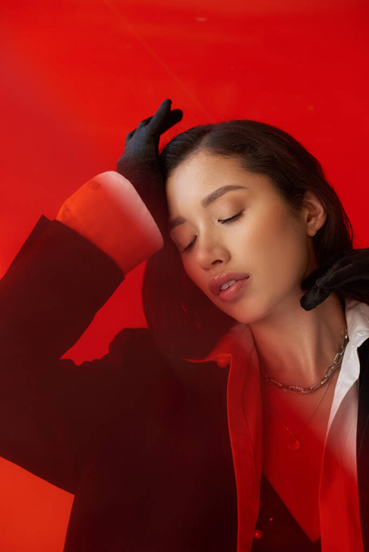 modernes Individuum, Modefotografie, junges asiatisches Model in weißem Hemd und Blazer posiert in Handschuhen auf rotem Hintergrund, geschlossene Augen, persönlicher Stil, Jugendtrend, konzeptionelle  - Foto, Bild