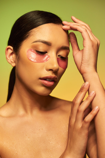 pretty and brunette asian woman posing with eye patches on green background, gradient, beauty, skin perfection, facial treatment, bare shoulders, skincare routine, glowing skin, portrait  - Photo, Image
