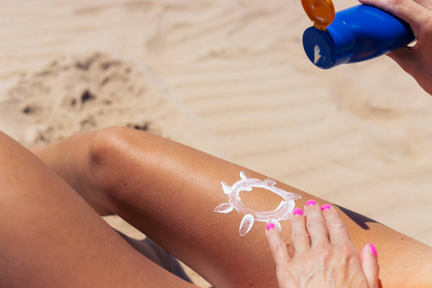 Großaufnahme einer Frauenhand, die Sonnencreme auf ihr Bein aufträgt. Hautpflege. Sonnenschutz. Eine Frau schmiert Sonnencreme mit feuchtigkeitsspendender Lotion auf ihre glatt gebräunten Beine. Hochwertiges Foto - Foto, Bild