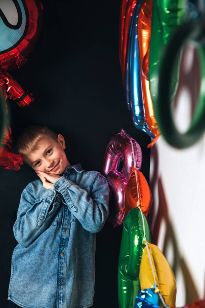 Celebração de aniversário das crianças. Um menino alegre, um estudante, com uma camisa azul no fundo de balões coloridos. Vista frontal - Foto, Imagem
