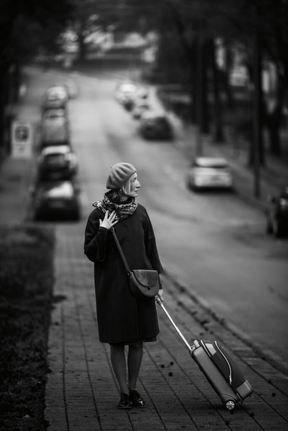 A woman with a suitcase is standing by the side of the road. Black and white photo. - Photo, image