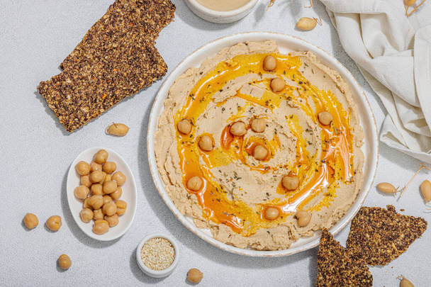 Hummus met olijfolie en knapperig brood. Onmisbaar ingrediënt voor een gezonde levensstijl. Comfort eten, veganistische snack. Hard licht, donkere schaduw, beton in steen, flat lay, bovenaanzicht - Foto, afbeelding