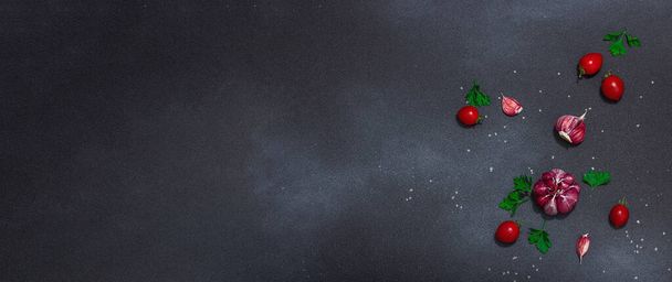 Fondo culinario con verduras y hierbas frescas. Tomates cereza, ajo, sal marina y perejil. Colocación plana, luz dura, sombra oscura, fondo de hormigón de piedra negra - Foto, Imagen