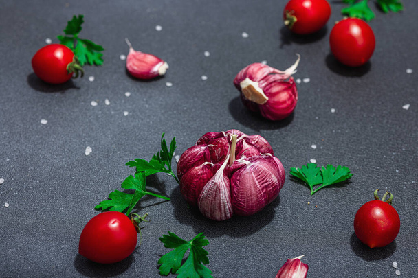 Culinary background with fresh vegetables and herbs. Tomatoes cherry, garlic, sea salt, and parsley. Flat lay, hard light, dark shadow, black stone concrete background - Foto, imagen
