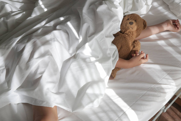 Kind slaapt onder witte lakens knuffelende teddybeer. Slaap tijd voor kinderen of bedtijd. - Foto, afbeelding