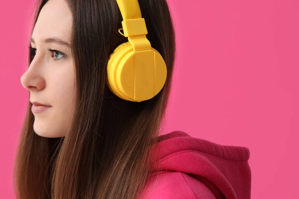Молода жінка в навушниках слухає музику на рожевому фоні
 - Фото, зображення