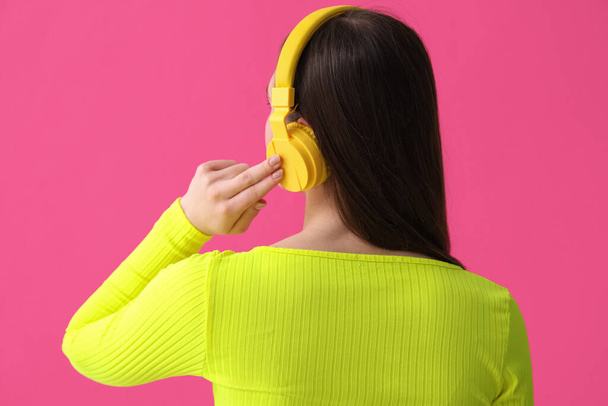 若いです女性でヘッドフォンで音楽を聴くピンクの背景 - 写真・画像