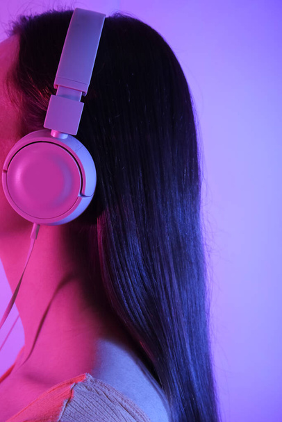 Young woman in headphones listening to music on color background - Фото, зображення