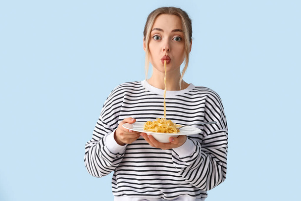 Young woman eating tasty pasta on blue background - Фото, изображение