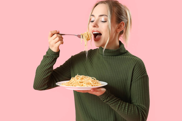 Young woman eating tasty pasta on pink background - Photo, image