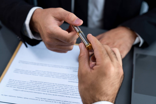 Two businesspeople sit across the desk as business deal is taking place. Corporate attorney giving a pen for client or partner to sign contract paper, sealing the deal with signature. Fervent - Zdjęcie, obraz