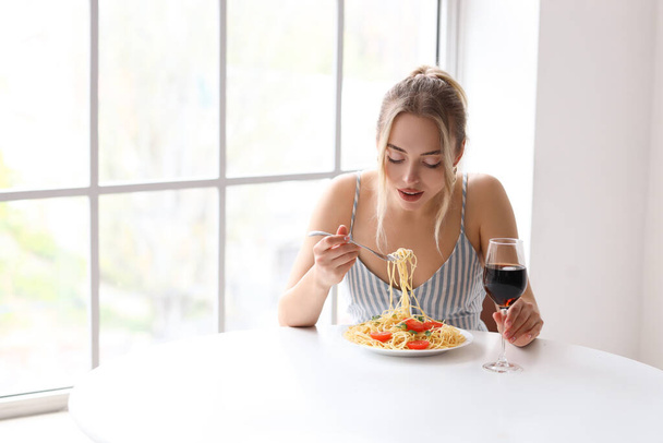 Jeune femme avec un verre de vin manger des pâtes savoureuses à table au restaurant - Photo, image