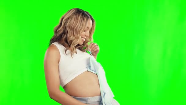 Βρεφικά ρούχα, ευτυχισμένη και έγκυος γυναίκα στην πράσινη οθόνη με την ανάπτυξη της κοιλιάς και την ανάπτυξη. Εγκυμοσύνη, ενθουσιασμένος πρόσωπο ή μητέρα με νεογέννητο γιλέκο προϊόν στην κρεμάστρα για να φανταστείτε μελλοντική επιλογή στολή. - Πλάνα, βίντεο